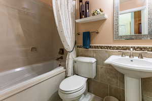 Bathroom featuring toilet, shower / bath combo with shower curtain, and tile walls