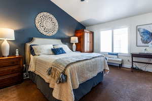 Bedroom featuring dark colored carpet and vaulted ceiling