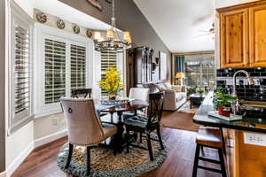 Dining space featuring lofted ceiling, ceiling fan with notable chandelier, dark hardwood / wood-style floors, and a textured ceiling