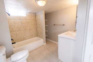 Full bathroom with tile patterned flooring, vanity, a textured ceiling, toilet, and tiled shower / bath