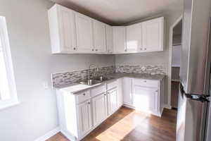 Kitchen with white cabinetry, sink, wood-type flooring, and stainless steel refrigerator