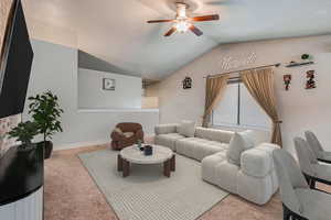 Carpeted living room featuring ceiling fan and lofted ceiling