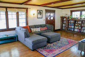 Living room featuring beam ceiling, wood window casings and hardwood flooring