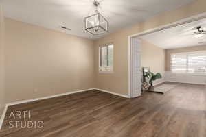 Unfurnished room with ceiling fan with notable chandelier, dark wood-type flooring, and a healthy amount of sunlight