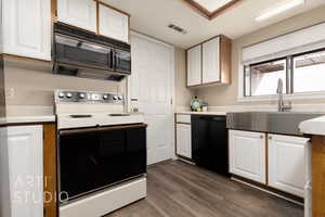 Kitchen with white cabinetry, sink, dark wood-type flooring, and black appliances