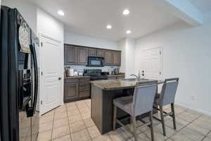 Kitchen featuring sink, light tile patterned floors, a breakfast bar, a kitchen island with sink, and black appliances