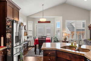 Kitchen with sink, stainless steel refrigerator with ice dispenser, light stone counters, dark  wood-style flooring, and vaulted ceiling