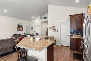 Kitchen featuring dark wood-type flooring, sink, vaulted ceiling, a kitchen breakfast bar, and a kitchen island with sink