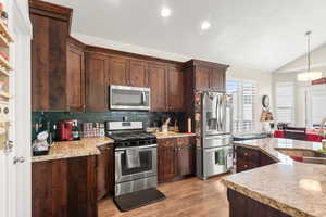 Kitchen with vaulted ceiling, sink, decorative light fixtures, stainless steel appliances, and light  wood-style floors