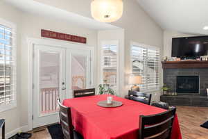 Dining area featuring a fireplace, wood-type flooring, french doors, and vaulted ceiling