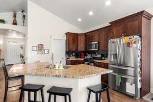 Kitchen with sink, wood-style flooring, a kitchen island with sink, stainless steel appliances, and light stone countertops