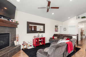 Living room with a tiled fireplace, wood-style flooring, vaulted ceiling, and ceiling fan