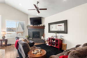 Living room featuring wood-style flooring, vaulted ceiling, ceiling fan, and a fireplace