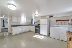 Kitchen featuring washer and dryer, white cabinets, white fridge, and black gas range oven