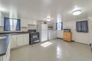 Kitchen featuring white cabinetry, white fridge, washing machine and clothes dryer, and black range with gas cooktop