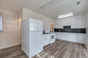 Kitchen featuring tasteful backsplash, white cabinetry, wood-type flooring, and white appliances