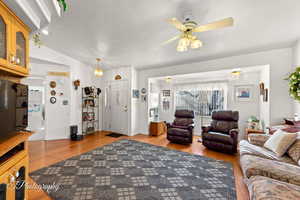 Living room with vaulted ceiling, ceiling fan, light hardwood / wood-style floors, and a textured ceiling