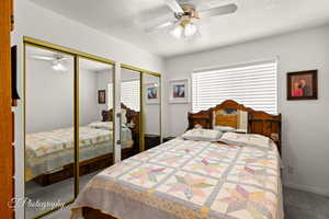 Carpeted bedroom with ceiling fan, two closets, and a textured ceiling