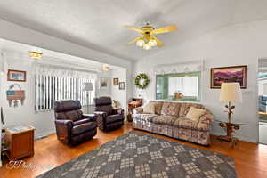 Living room featuring ceiling fan, vaulted ceiling, light hardwood / wood-style flooring, and a textured ceiling