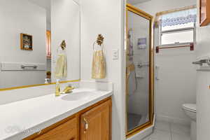 Bathroom with a shower with door, vanity, tile patterned floors, and toilet