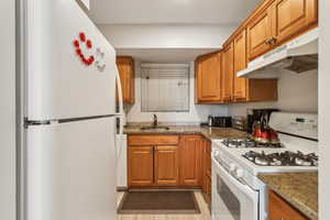 Kitchen featuring light stone counters, white appliances, and sink