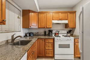 Kitchen featuring light stone counters, sink, and white appliances