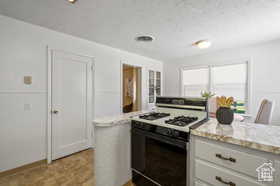 Kitchen with white cabinetry, light stone countertops, range with gas stovetop, and a textured ceiling