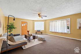 Carpeted living room featuring ceiling fan and a textured ceiling