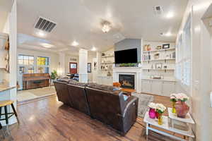 Living room with light hardwood / wood-style flooring, decorative columns, a textured ceiling, built in shelves, and vaulted ceiling