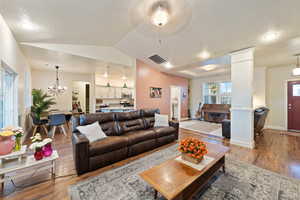 Living room featuring vaulted ceiling, a chandelier, decorative columns, and hardwood / wood-style floors