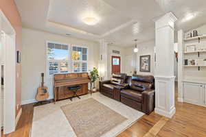 Living room with light hardwood / wood-style floors, decorative columns, a raised ceiling, and a textured ceiling