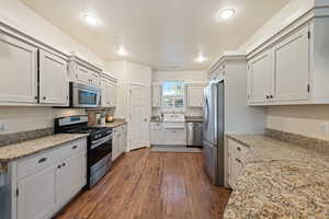 Kitchen featuring white cabinetry, appliances with stainless steel finishes, light stone countertops, and dark wood-type flooring