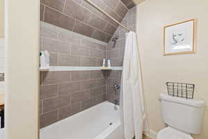 Bathroom with vaulted ceiling, shower / bath combination with curtain, and toilet