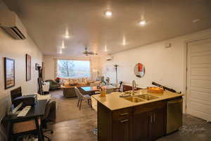 Kitchen with sink, dark brown cabinets, a center island with sink, stainless steel dishwasher, and a wall unit AC