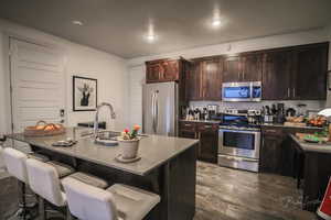 Kitchen featuring a kitchen bar, sink, dark brown cabinets, stainless steel appliances, and a kitchen island with sink