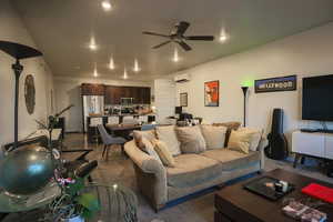 Carpeted living room featuring ceiling fan and a wall mounted air conditioner