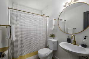 Bathroom featuring a shower with shower curtain, toilet, and sink