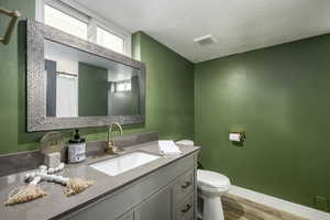 Bathroom with walk in shower, toilet, a textured ceiling, vanity, and hardwood / wood-style floors