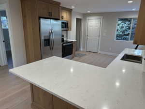 Kitchen with sink, light wood-type flooring, light stone countertops, and appliances with stainless steel finishes