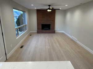 Unfurnished living room featuring a brick fireplace, ceiling fan, and light wood-type flooring