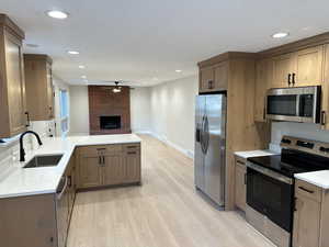 Kitchen featuring sink, light hardwood / wood-style flooring, stainless steel appliances, a brick fireplace, and kitchen peninsula