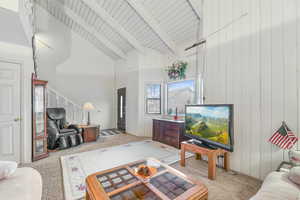 Living room featuring wood ceiling, high vaulted ceiling, wooden walls, light colored carpet, and beam ceiling