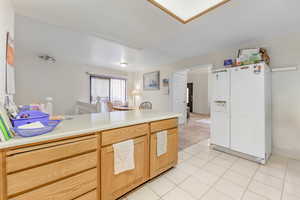 Kitchen featuring light tile patterned flooring, white refrigerator with ice dispenser, and light brown cabinets