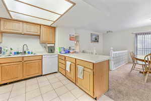 Kitchen featuring white dishwasher, sink, light tile patterned floors, and kitchen peninsula