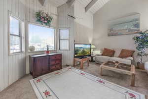 Living room featuring vaulted ceiling with beams, light colored carpet, wooden ceiling, and wooden walls