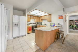 Kitchen featuring sink, a breakfast bar area, light tile patterned floors, kitchen peninsula, and white appliances