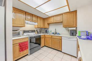 Kitchen featuring range with electric cooktop, white dishwasher, sink, and light tile patterned floors