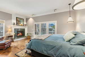 Bedroom featuring ornamental molding, wood-type flooring, a fireplace, and access to outside