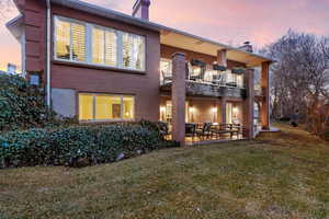 Back house at dusk featuring a balcony, a yard, and a patio