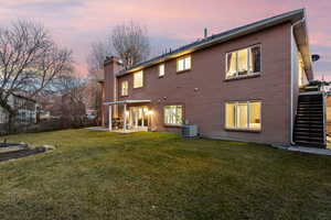 Back house at dusk with cooling unit, a patio area, and a lawn